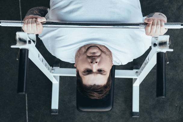 Κορυφαία θέα του υπέρβαρου άνδρα σε λευκό t-shirt εκπαίδευση με μπάρα στο γυμναστήριο - Φωτογραφία, εικόνα