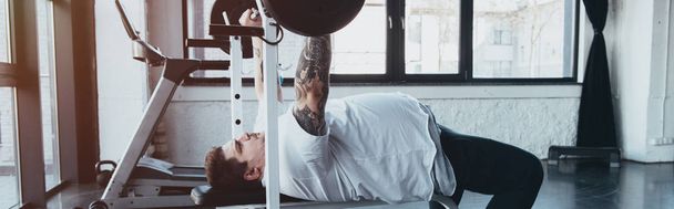 panoramic shot of Overweight tattooed man training with barbell at gym - Photo, Image