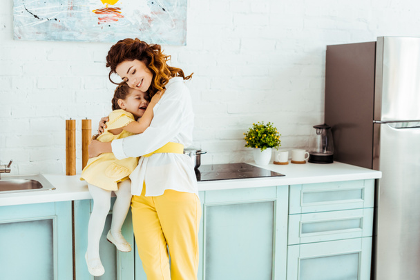 happy mother embracing cute daughter in kitchen - Фото, изображение