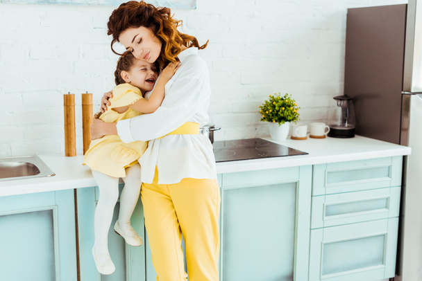 happy mother embracing excited daughter in kitchen - Photo, Image