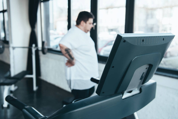 selective focus of treadmill and overweight man looking through window at sports center - Valokuva, kuva