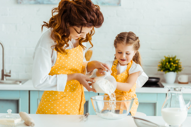 matka pomáhající dceři přidat mouku do mísy v kuchyni - Fotografie, Obrázek