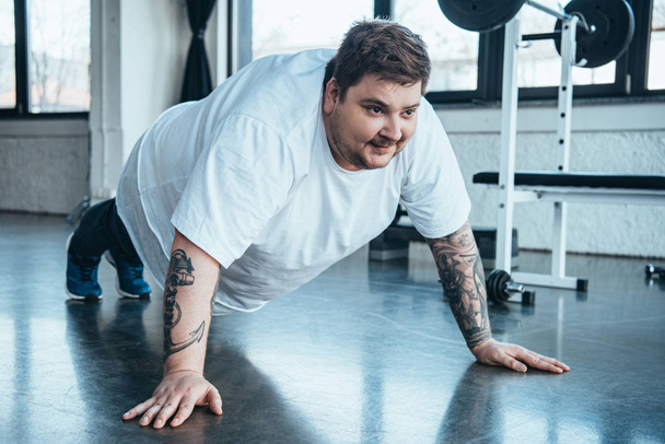 толстый татуированный мужчина делает упражнения на отжимание в спортивном центре
 - Фото, изображение
