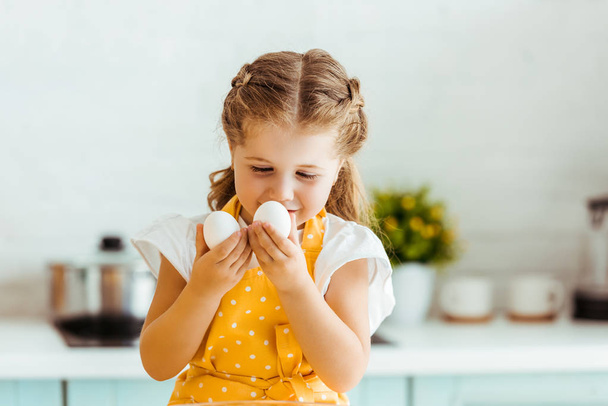 cute kid in yellow polka dot apron looking at eggs in kitchen - Foto, Imagen