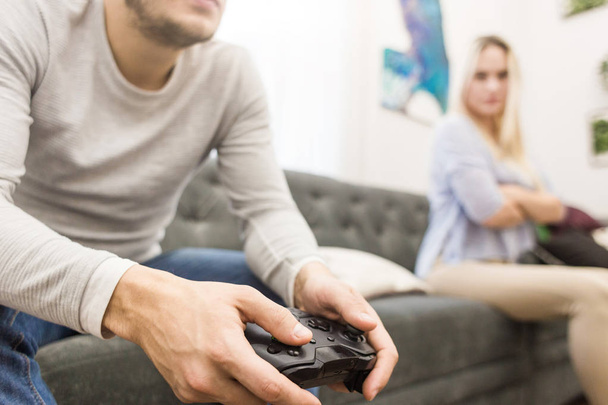A man holds a gamepad in his hands, a disgruntled girl sits next to them, they quarrel. - Photo, image