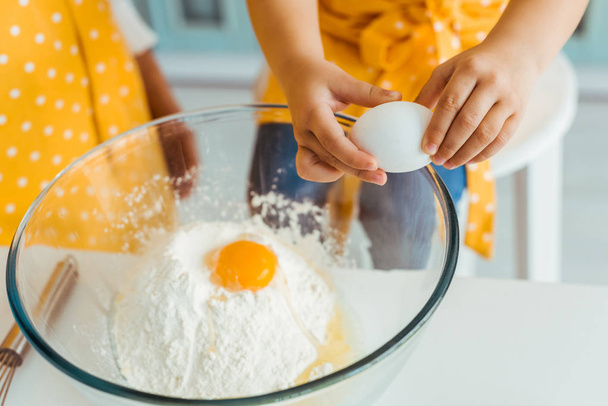 vista cortada da criança adicionando ovos à farinha em tigela de vidro
 - Foto, Imagem