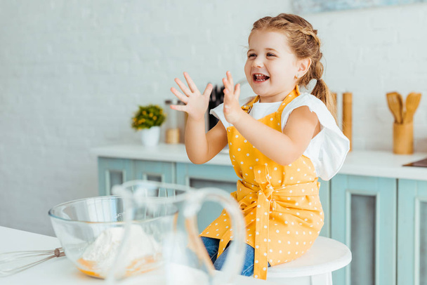 emotional kid in yellow polka dot apron gesturing in kitchen - Photo, Image