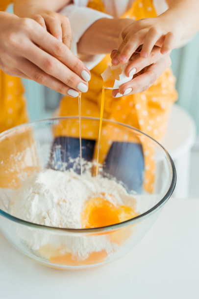 cropped view of mother and daughter smashing egg into bowl with flour - Photo, Image