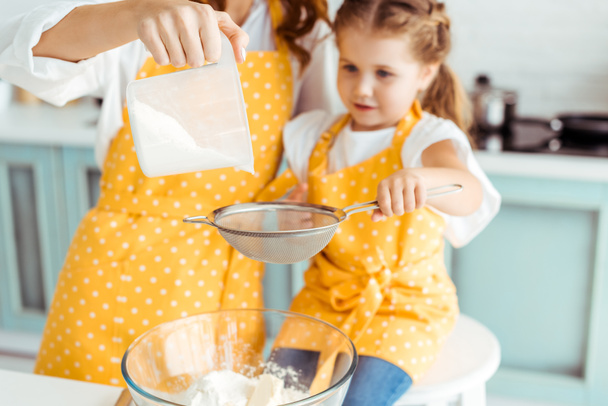 selective focus of mother and daughter sieving flour together into bowl - 写真・画像