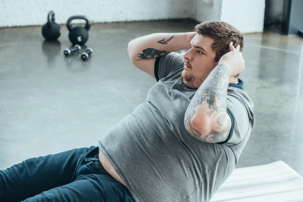 overweight tattooed man doing sit up exercise at sports center - Фото, изображение