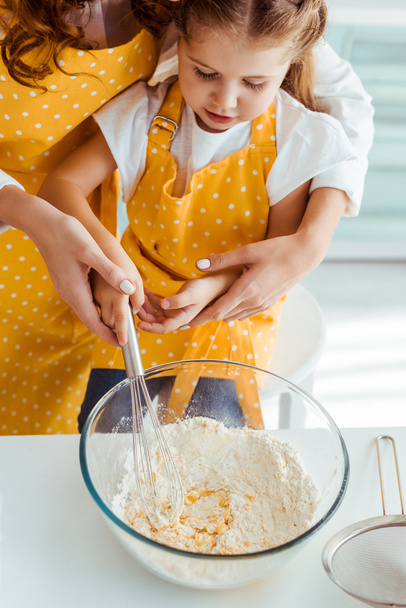mother and daughter in aprons mixing flour and eggs with balloon whisk in bowl - Foto, Imagen