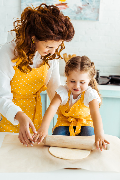 onnellinen äiti auttaa tytärtä rullaamalla taikina leivontaan pergamentti paperi
 - Valokuva, kuva