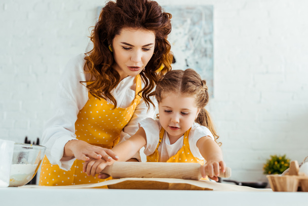 young mother helping daughter rolling out dough on baking parchment paper - Foto, immagini