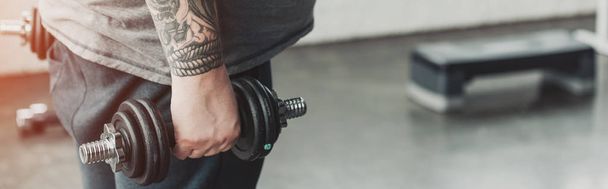 panoramic shot of Overweight tattooed man training with dumbbell at gym with copy space - Photo, Image