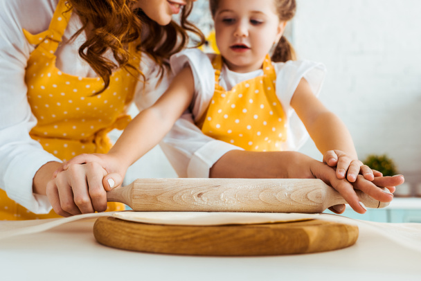 selective focus of mother and daughter rolling out dough with wooden rolling pin on baking parchment paper - Photo, Image