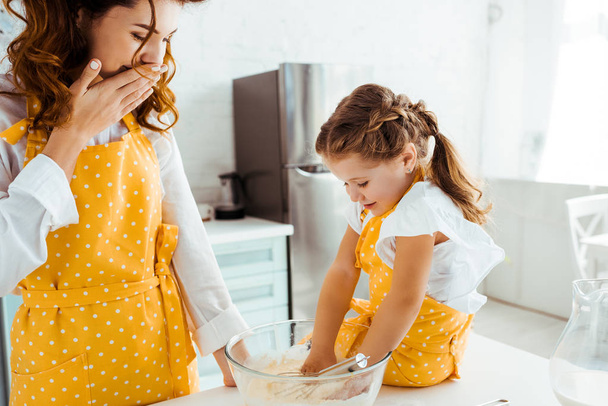 Schockierte Mutter schaut Tochter an, wie sie Hände in Schüssel mit Mehl legt - Foto, Bild