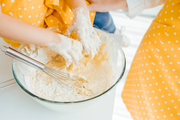 cropped view of kid putting hands in bowl with raw dough and balloon whisk - Foto, Imagen