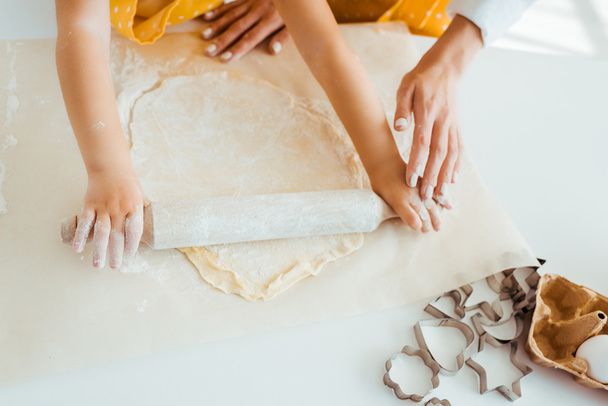 top view of mother and daughter rolling out dough near dough molds on table - Foto, Imagem