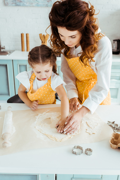 madre e hija en delantales de lunares amarillos usando moldes de masa en la cocina
 - Foto, Imagen