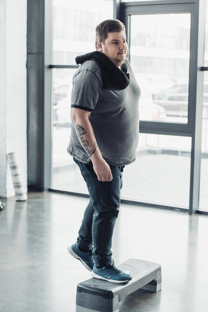 человек с избыточным весом с полотенцем тренировки на ступенчатой платформе в тренажерном зале
 - Фото, изображение
