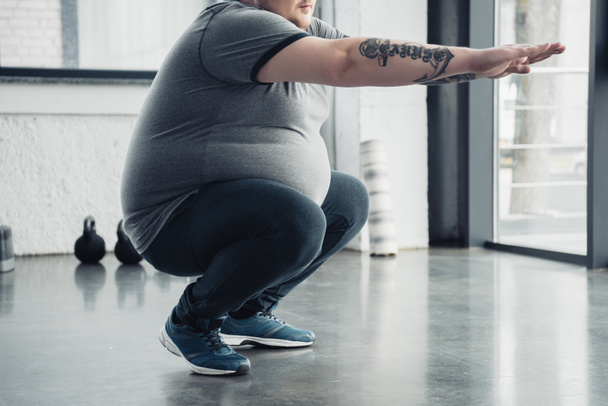 cropped view of overweight tattooed man doing squats at sports center - Foto, Bild