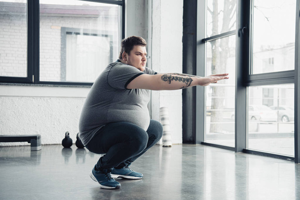 overweight tattooed man doing squats at sports center - Foto, Imagen