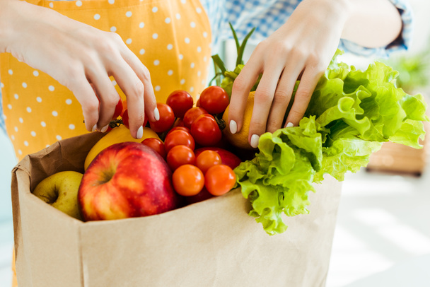 partial view of woman touching fresh ripe fruits and vegetables in paper bag - Photo, Image