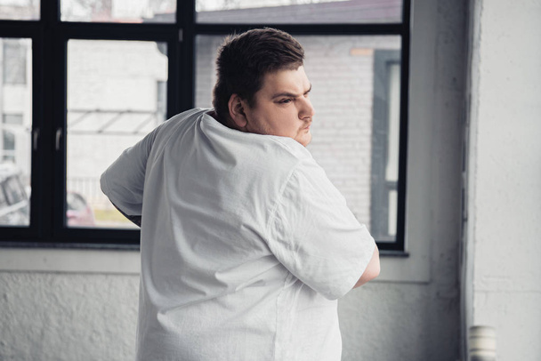overweight tattooed man in white t-shirt stretching at gym - Fotografie, Obrázek