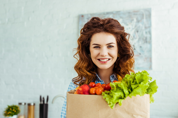 lachende mooie vrouw die papieren tas met rijpe verse groenten houdt - Foto, afbeelding