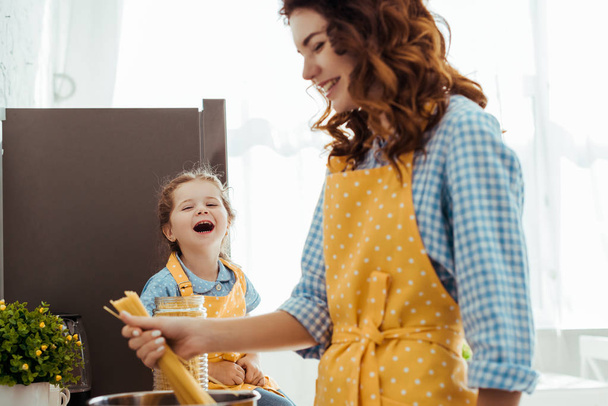 smiling mother holding raw spaghetti near laughing excited daughter - Photo, Image