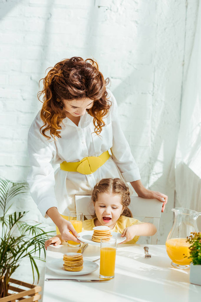 mother giving excited daughter pancakes for breakfast - Foto, Imagem