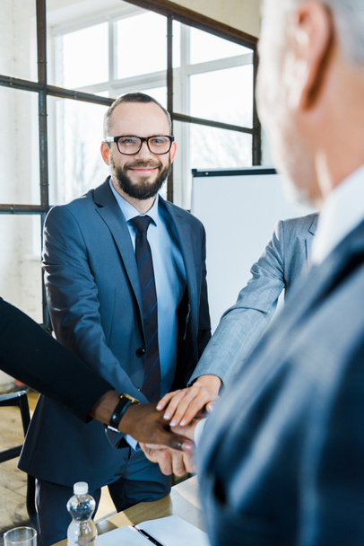 happy bearded man putting hands together with multicultural coworkers in conference room  - Photo, Image