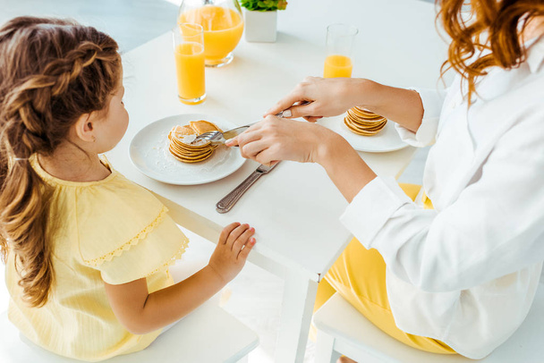 partial view of mother cutting pancakes with fork and knife near daughter  - Φωτογραφία, εικόνα