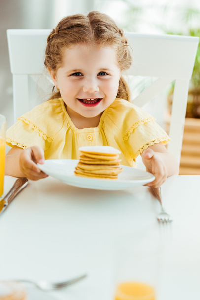 selective focus of smiling child holding plate with sweet pancakes - Zdjęcie, obraz
