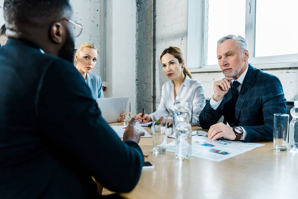 businesswomen and businessman looking at african american coworker in conference room  - Foto, Imagem