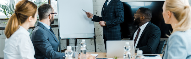 panoramic shot of business coach pointing at white board with pen near multicultural coworkers  - Photo, Image