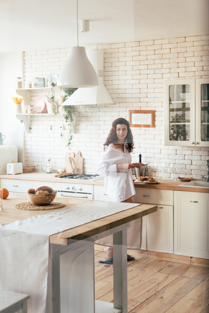 Krásná žena v bílé košili, která při přípravě snídaně v kuchyni hledí - Fotografie, Obrázek