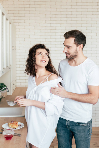 smiling girl looking at boyfriend while preparing breakfast in kitchen - 写真・画像