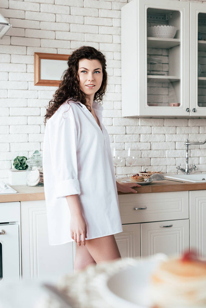 dreamy young woman in white shirt looking away with smile in kitchen - Фото, изображение