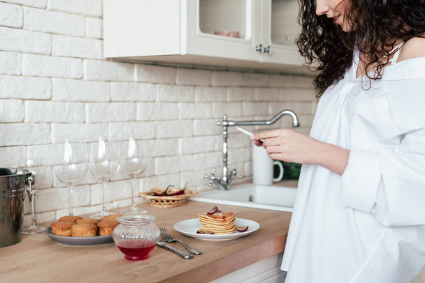 partial view of pretty girl in white shirt using smartphone in kitchen - Photo, Image