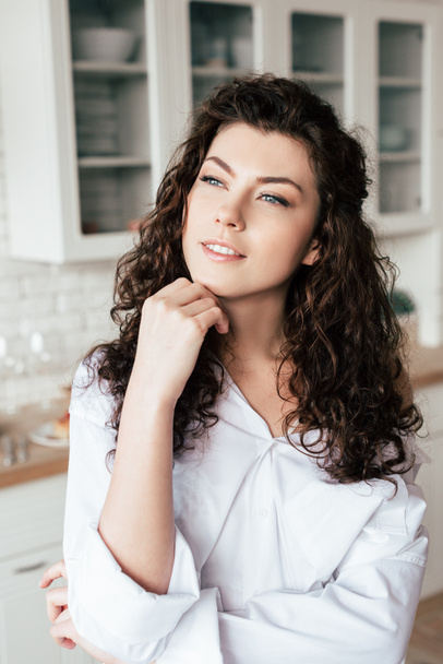 dreamy young woman with curly hair looking away in kitchen - Фото, изображение