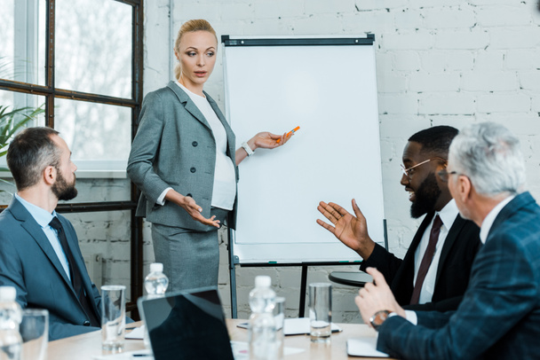 Enceinte blonde coach d'affaires debout près du tableau blanc et gestuelle dans la salle de conférence
  - Photo, image