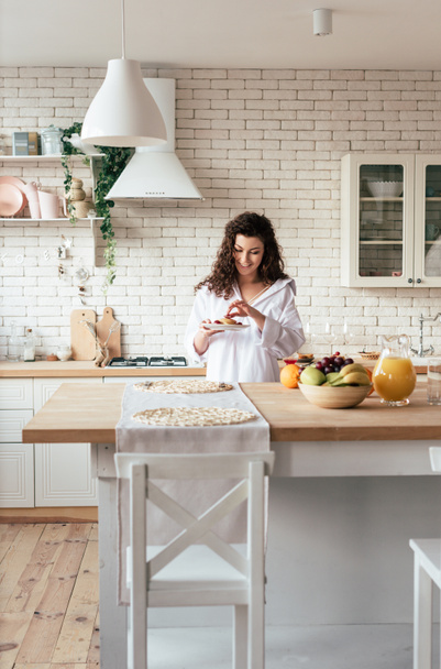 Lächelnde junge Frau im Hemd isst Pfannkuchen in der Küche - Foto, Bild