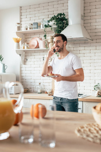 bearded man talking on smartphone with smile and holding plate with pancakes  - Foto, Imagem