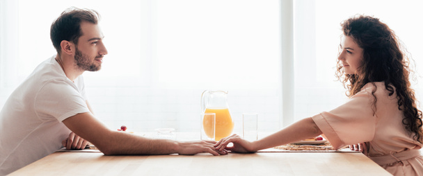 panoramic shot of couple touching hands and looking at each other during breakfast - Фото, изображение
