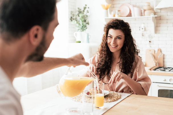 partial view of man pouring orange juice in glass while sitting at table with girlfriend - Photo, Image