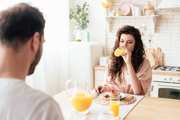 mujer rizada bebiendo jugo de naranja mientras está sentada en la mesa con su novio
 - Foto, imagen
