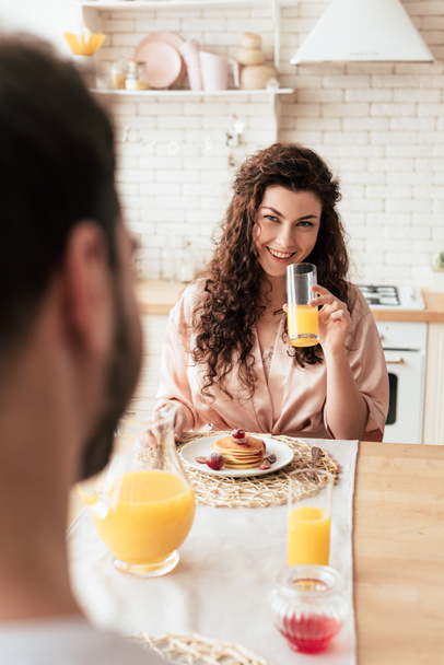 laughing girl holding glass of juice while sitting at table with boyfriend - Photo, Image