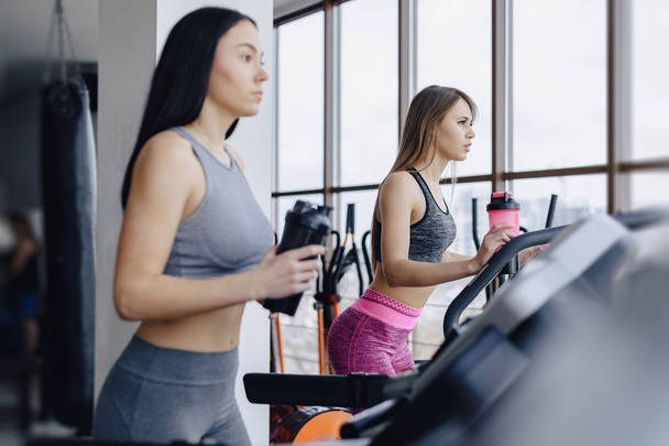 Girls in the gym are trained on treadmills and drink water, smiling - Photo, Image