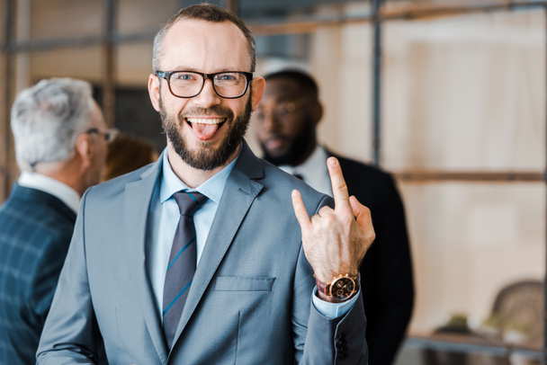 selective focus of happy businessman showing tongue and rock sign near multicultural coworkers  - Φωτογραφία, εικόνα